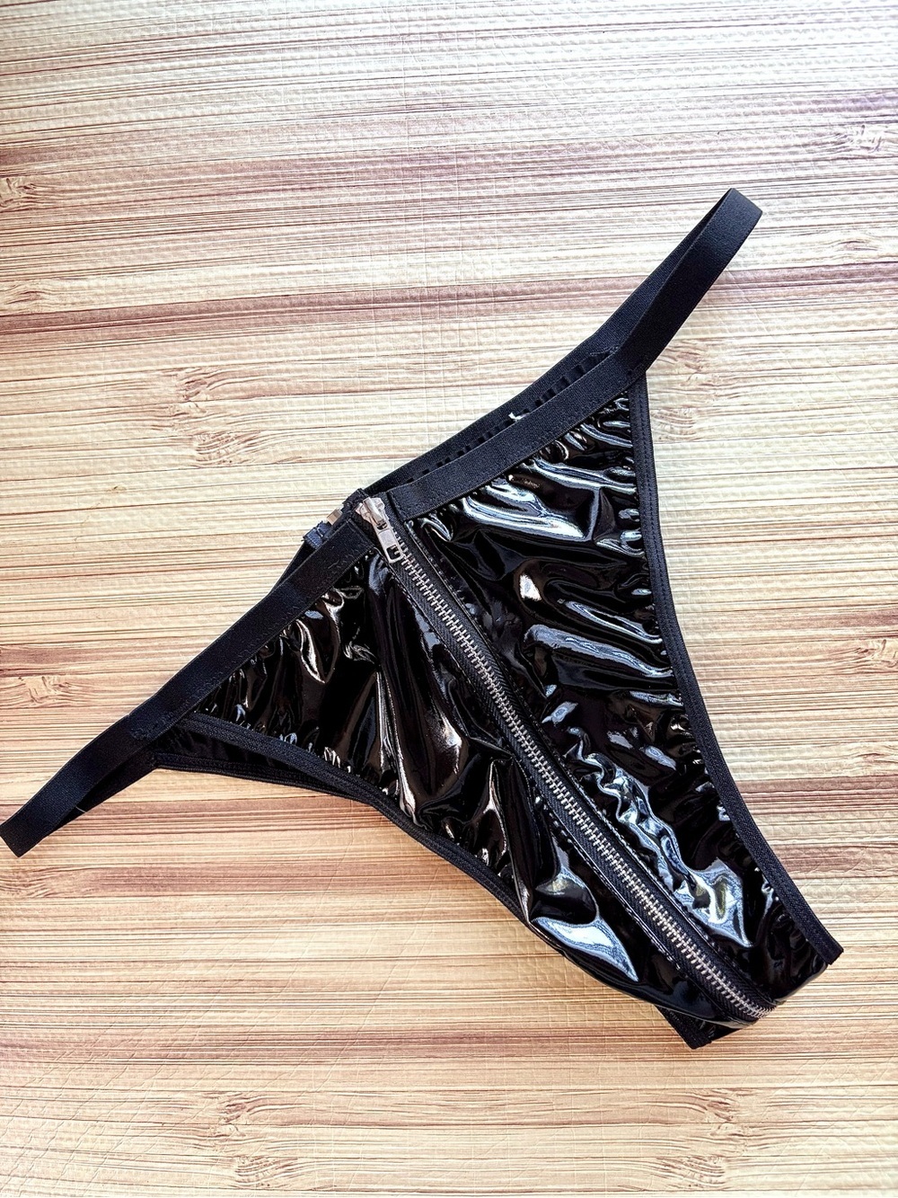 shiny black faux leather thong features a prominent front-to-back zipper closure